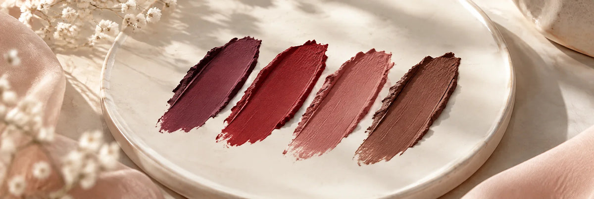 Four rich matte lipstick pigment strokes in plum, red, rose and cocoa on ivory ceramic, beautifully soft velvety texture.