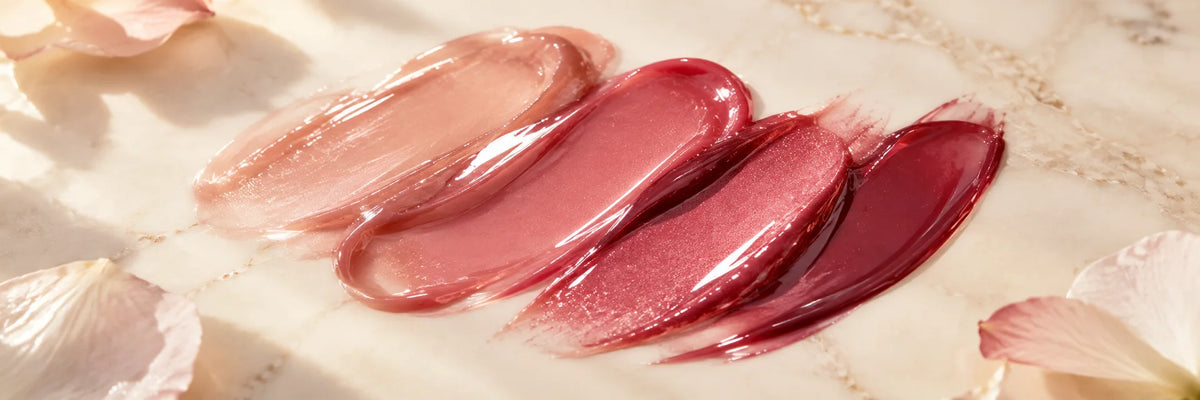 Ultra-glossy sheer rose and berry cosmetic swatches with beautiful soft highlights on ivory porcelain, luminous premium lip-gloss texture still life.
