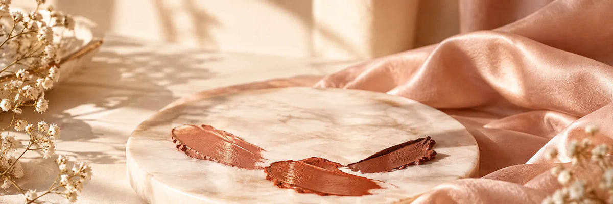 Warm terracotta, caramel nude and cinnamon brown lipstick textures on ivory porcelain and soft blush silk, subtle golden daylight.